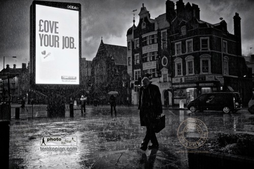 Love Your Job: A heavy downpour of rain soaks pedestrians as they pass an illuminated advertising sign saying "Love Your Job". Hammersmith, London. January 14, 2011. Photo: ©Edmond Terakopian